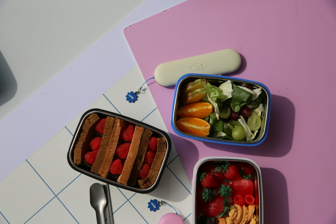 Three stainless lunchboxes packed with sandwiches, salad and fruit